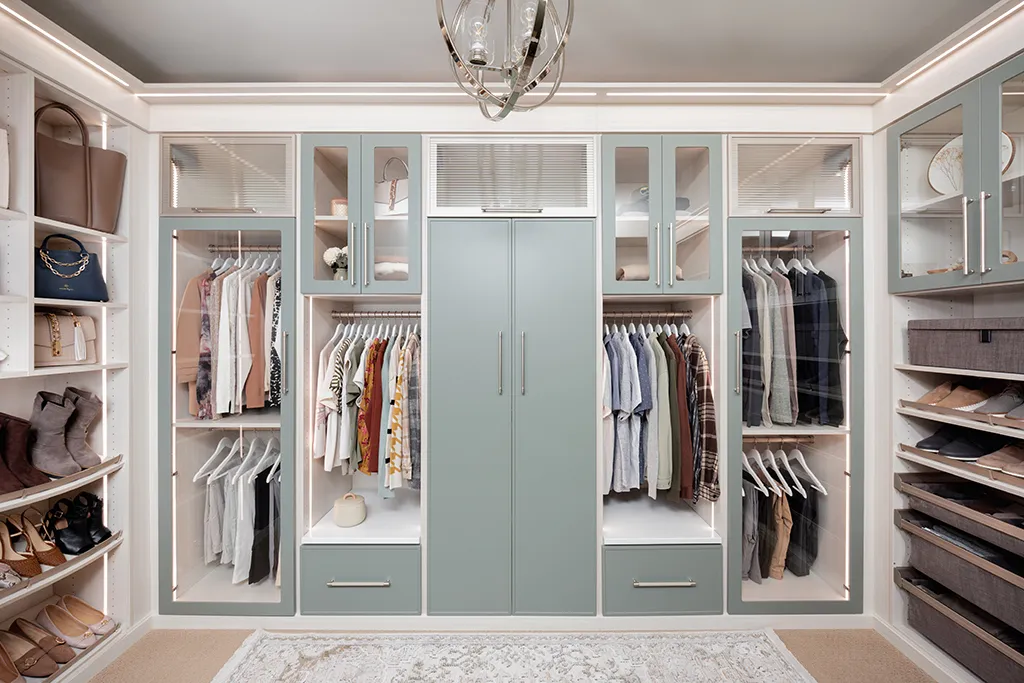 Bright white and sage custom walk-in closet with glass doors, drawers, clothing, shoes, and integrated lighting.