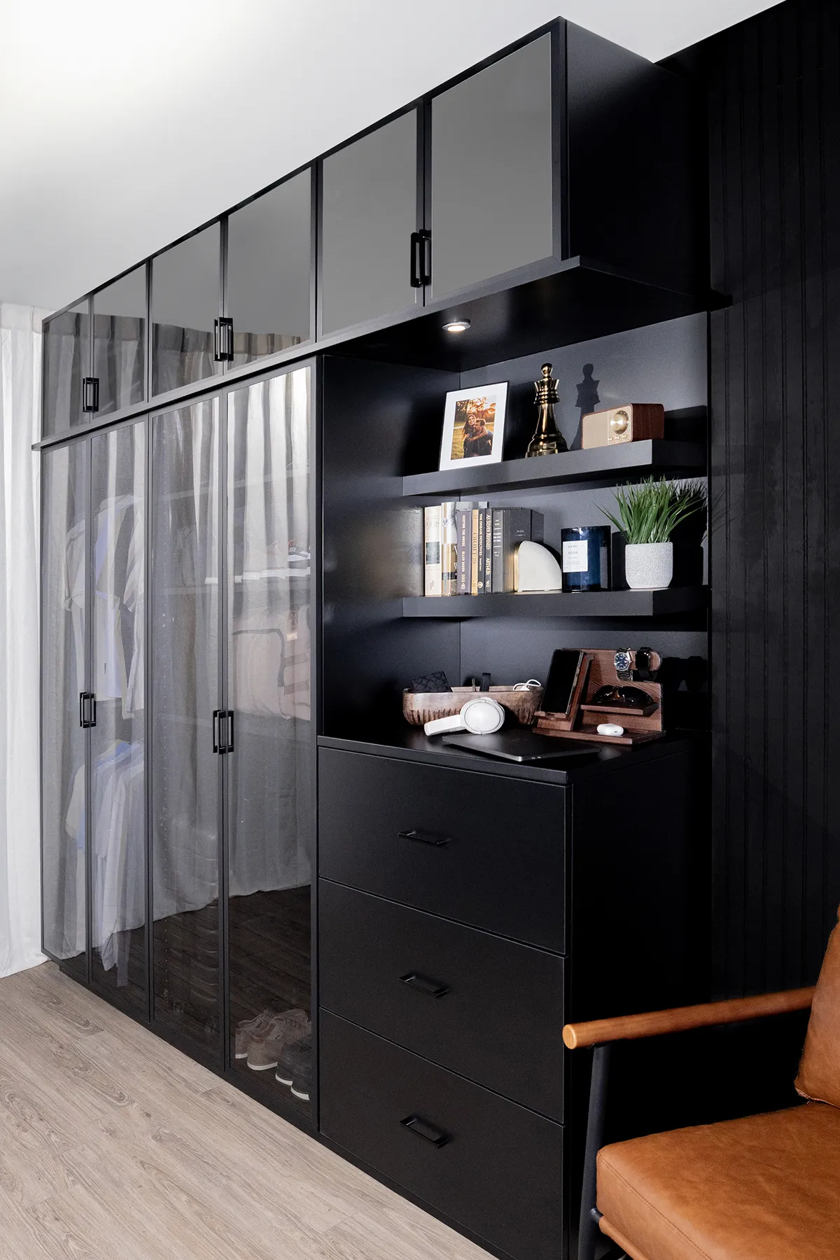 Matte-black storage wall with tinted glass wardrobe doors, upper cabinets, display shelves, and deep drawers.