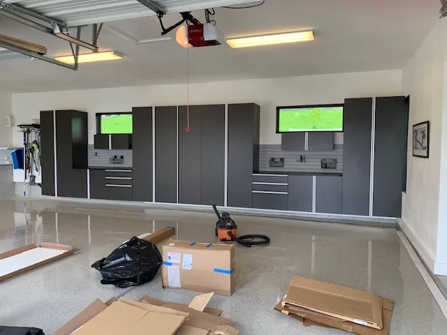 Gray garage storage cabinets and work counters with installation boxes and a vacuum on a glossy floor.