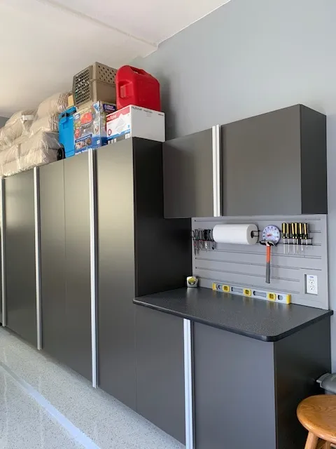 Dark gray garage cabinets with a black worktop, slatwall tool storage, and upper cabinets.